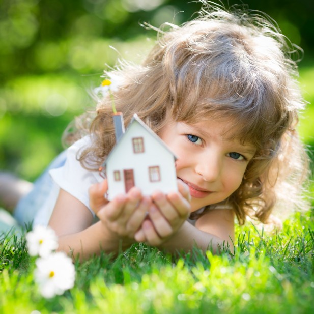 Ecology house in childrens hands against spring green background
